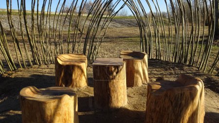 Foto de Mesa y asientos hechos de troncos de árbol y una cabaña hecha de ramas. - Imagen libre de derechos