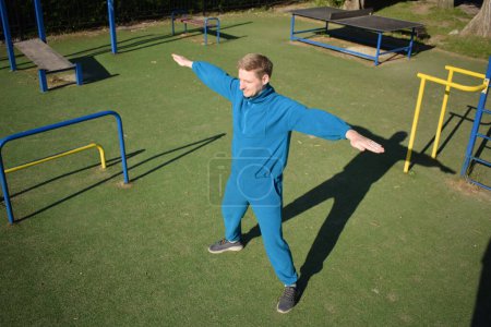 Un joven atleta enfocado realiza dinámicamente ejercicios de calentamiento y se estira al aire libre. Vestido con equipo deportivo, prepara meticulosamente el cuerpo para las demandas físicas que se avecinan a través de una rutina reglada.