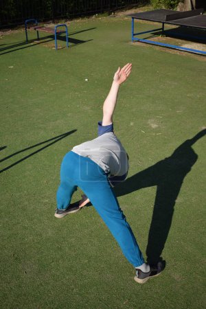 Un joven atleta enfocado realiza dinámicamente ejercicios de calentamiento y se estira al aire libre. Vestido con equipo deportivo, prepara meticulosamente el cuerpo para las demandas físicas que se avecinan a través de una rutina reglada.
