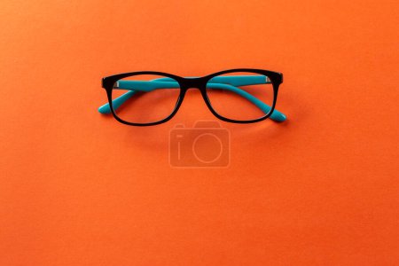 Téléchargez les photos : Stylish eyeglasses over orange background. Optical store, glasses selection, eye test, vision examination at optician, fashion accessories concept. Top view, flat lay - en image libre de droit