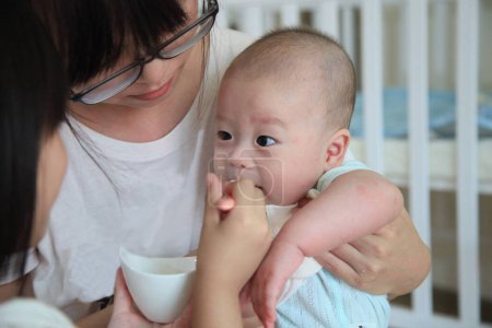 Foto de Asiática hermanos cuidando hermana ayuda alimentar bebé en un cariñoso familia escena - Imagen libre de derechos