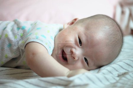 Téléchargez les photos : Asiatique bébé garçon sourit sur confortable lit - en image libre de droit
