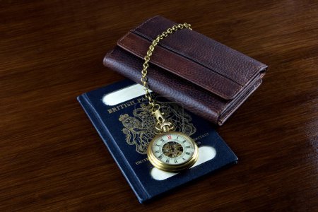 Photo for Old pocket watch with leather wallet and vintage UK passport on a wooden table top - Royalty Free Image