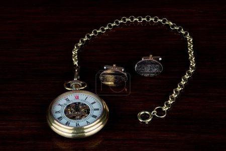 Photo for Gold cuff links and vintage pocket watch on a polished wooden surface - Royalty Free Image