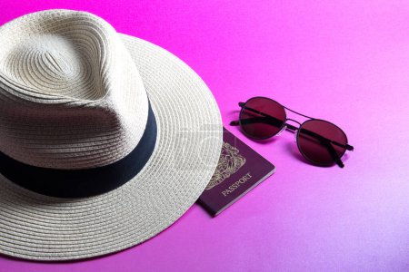 Straw panama hat with passport and sunglasses isolated on a pink background
