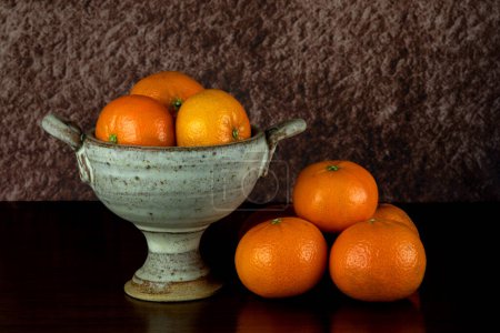 Téléchargez les photos : Bol à calice en terre cuite avec oranges satsuma sur une surface en bois poli - en image libre de droit