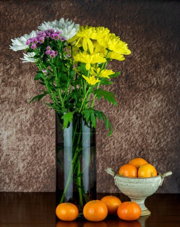 Téléchargez les photos : Fleurs de chrysanthème assorties dans un vase en verre sur une surface en bois avec bol de calice en poterie et oranges satsuma - en image libre de droit
