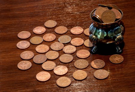 Copper coins and old silver pot on a varnished wooden table top