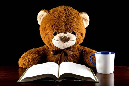 Großer brauner Teddybär sitzt an einem Tisch und liest mit einer Tasse Kaffee oder Tee