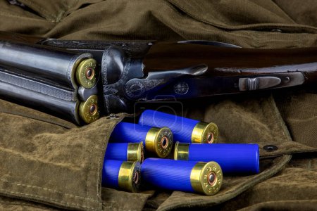 Téléchargez les photos : Cartouches de fusil de chasse se déversant de la poche ouverte d'un manteau de plein air avec un fusil de chasse vintage - en image libre de droit
