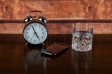 Reloj despertador con vaso de agua y teléfono móvil en un estante de madera