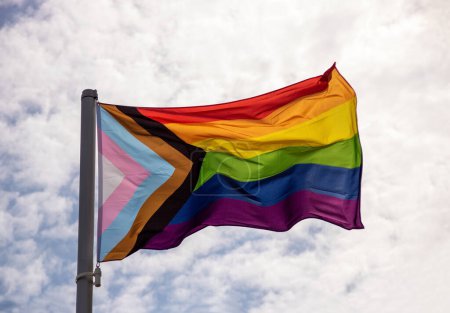 Gay pride flag fluttering in the breeze against a cloudy summer morning sky