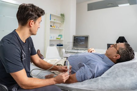 Photo for Concentrated physiotherapist performs an ultrasound on the arm of a lying patient while looking at the machine - Royalty Free Image