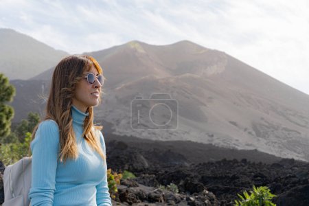Photo for Woman with sunglasses in front of the Tajogaite volcano viewpoint, with the volcano out of focus in the background, in La Palma island - Royalty Free Image