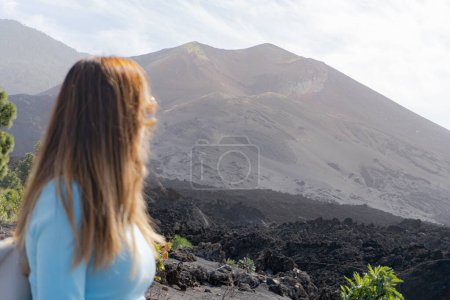 Photo for Woman with sunglasses looks at the tajogaite volcano from a viewpoint, she is seen from behind and out of focus in the foreground, in La Palma island - Royalty Free Image