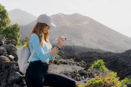 Photo for Woman with a cap looks at her sunglasses at the Tajogaite volcano viewpoint, sideways, on the island of La Palma, volcano in the background, backpacker - Royalty Free Image