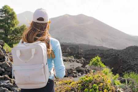 Photo for Woman with her back and with a cap looks towards the Tajogaite volcano from a viewpoint on the island of La Palma, backpacker - Royalty Free Image