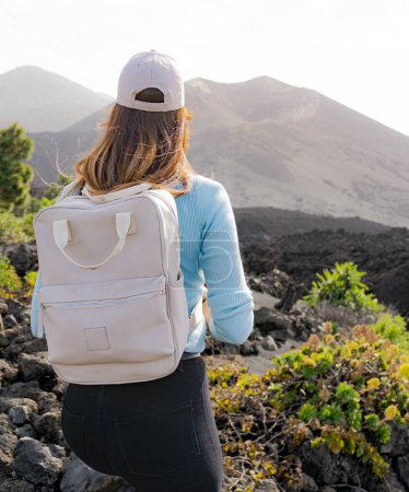 Photo for Woman with her back and with a cap looks towards the Tajogaite volcano from a viewpoint on the island of La Palma, vertical shot, backpacker - Royalty Free Image