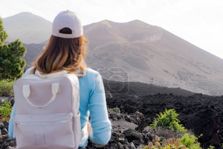 Photo for Close-up female backpacker with cap on her back looks towards the Tajogaite volcano from a viewpoint on the island of La Palma - Royalty Free Image