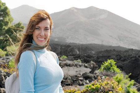 Photo for Backpacker woman smiles looking at the camera at the Tajogaite volcano, the volcano is seen out of focus in the background, on the island of La Palma - Royalty Free Image