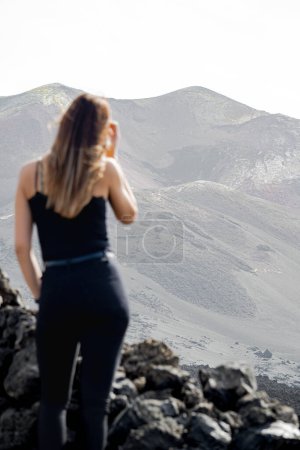 Photo for Woman standing from behind, looking at the Tajogaite volcano from a viewpoint, placing her hair, on the island of La Palma, vertical shot - Royalty Free Image