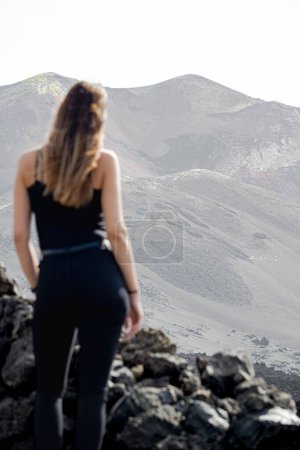 Photo for Woman standing from behind, looking at the Tajogaite volcano from a viewpoint, on the island of La Palma, vertical shot - Royalty Free Image