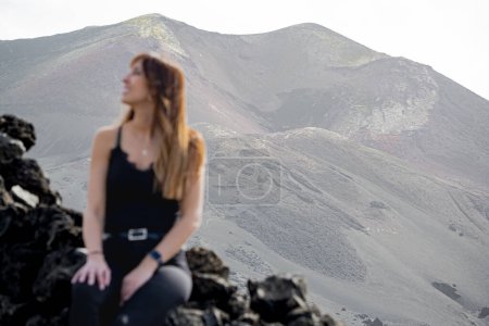 Photo for Woman in suspenders looks at the sky smiling in front of the Tajogaite volcano, she is seen out of focus in the foreground, at a viewpoint on the island of La Palma - Royalty Free Image