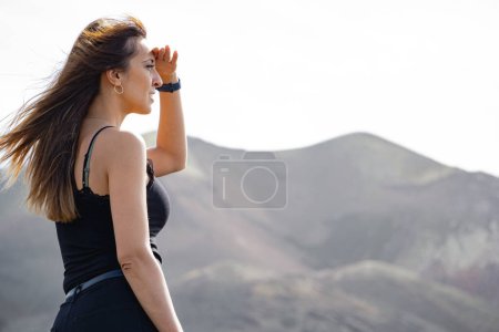 Photo for Close-up woman covering the sun from her face in front of the Tajogaite volcano, at a viewpoint on the island of La Palma, with her hair flying in the wind - Royalty Free Image