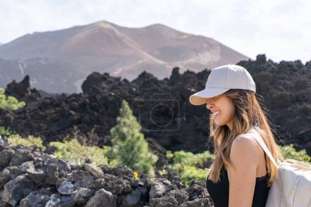 Photo for Close-up woman with cap walks smiling looking at the ground in front of the Tajogaite volcano viewpoint, on the island of La Palma - Royalty Free Image