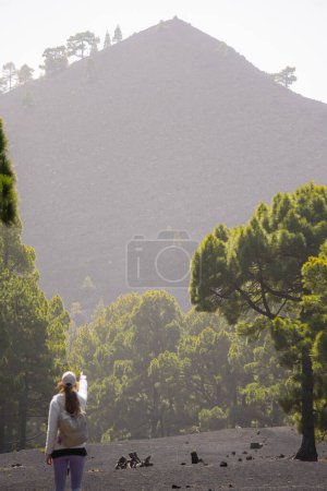 une femme debout sur une plaine au milieu de la forêt pointe vers le sommet d'un volcan à La Palma, îles Canaries, plan vertical