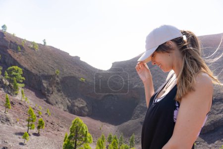Femme souriante tenant sa casquette dans le cratère d'un volcan à La Palma dans les îles Canaries, les cheveux soufflés par le vent
