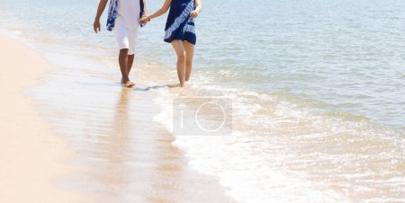 Photo for An outdoor photo of a romantic young couple walking along the seashore holding hands. a young man and a woman walking on the beach together - Royalty Free Image