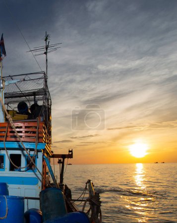 Photo for A photograph of a fisherman boat in a rippling sea background with the sun rising from the horizon in beautiful light and signifying the start of a new day or an exciting journey or adventure by boat. - Royalty Free Image