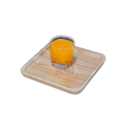 Photo for A clear glass of orange juice is placed on a wooden tray with a white background. - Royalty Free Image
