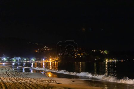 Photo for On the beach at night, the sea is pounding, and on the mountains the lights of residential and hotel accommodations are lit up. - Royalty Free Image