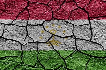 Téléchargez les photos : Tajikistan flag on a mud texture of dry crack on the ground - en image libre de droit