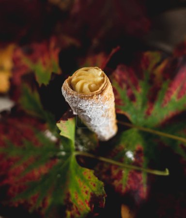 Téléchargez les photos : Gâteau feuilleté en forme de cône rempli de crème tenue par des feuilles d'automne - en image libre de droit