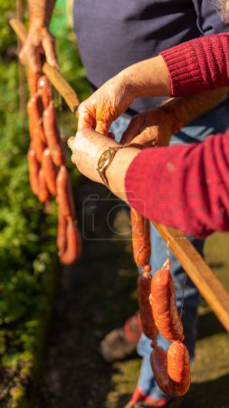 Photo for Human hands hold a wooden stick where they hang sausages to place them in a dry and smoky place for healing and conservation - Royalty Free Image