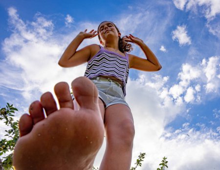 Téléchargez les photos : Teen woman walks barefoot through the garden and raises her hands to the blue sky dappled with white clouds - en image libre de droit