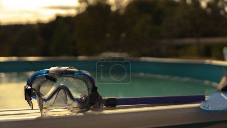 Foto de Gafas de buceo para niños colocadas en el borde de una piscina en una puesta de sol de verano - Imagen libre de derechos