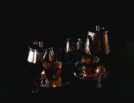 Dos tazas de vidrio llenas de té en placas de metal plateado con recipientes para almacenar el líquido
