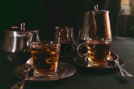 Dos tazas de vidrio llenas de té en placas de metal plateado con recipientes para almacenar el líquido