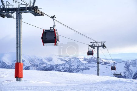 Photo for Cable car gondola at a ski resort with snowy mountains on background. Modern ski lift with funitels and supporting towers high in the mountains on winter day. No people. - Royalty Free Image