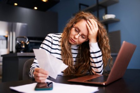 Unhappy woman calculates expenses on bills, upset about increased utilities prices. Female counting paychecks, debts, loans, reciepts to pay taxes. Inflation, low paying capacity, financial crisis.