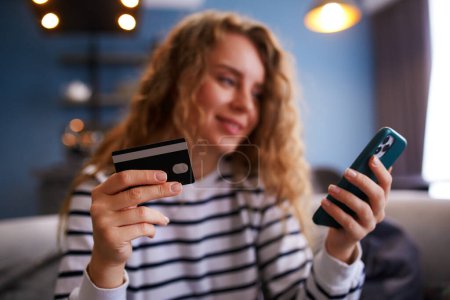 Photo for Happy woman makes purchase, payment in fintech app on phone. Shopper girl uses mobile banking app, credit card to pay for goods in internet store. Female in anticipation of order fullfilment. - Royalty Free Image