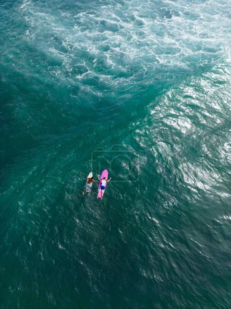 Téléchargez les photos : Drone shot de surfeurs sur des planches de surf s'entraînant en mer bleue. Vue aérienne des amateurs d'eau s'engageant avec le surf puissant. - en image libre de droit