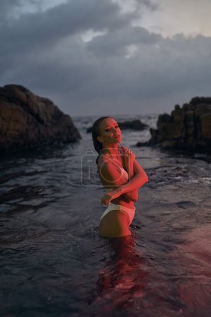 Photo for Beautiful lady takes a nighttime dip in sea illuminated by red light, capturing travel and relaxation theme, tranquility in marine setting, vacation beauty experience, serene coast exploration. - Royalty Free Image