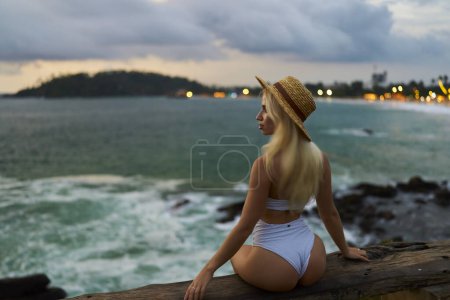 Female traveler contemplates tranquil seascape from rocky shore, enjoying solitude and natural beauty during twilight, embodying mindfulness and peaceful escape