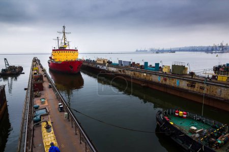 Vessel maintenance at shipyard, maritime logistics. Icebreaker ship enters floating dock, marine engineering prowess. Shipping industry operates in drydock, nautical repair expertise.