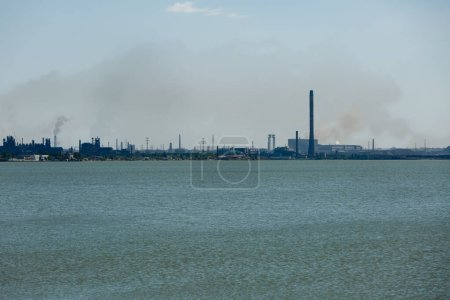 Fabrikverschmutzung, Umweltbedenken und Auswirkungen der Schwerindustrie auf den gesamten See. Industrielle Skyline, die von metallurgischen Anlagen über dem Wasser dominiert wird und Rauch in den Himmel abgibt.